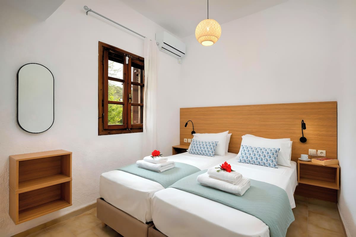 A double bed with a wooden headboard, two bedside tables with lamps, a small shelf, and a window with curtains.