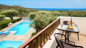 A balcony with a table set for two, overlooking a swimming pool and a view of the sea.