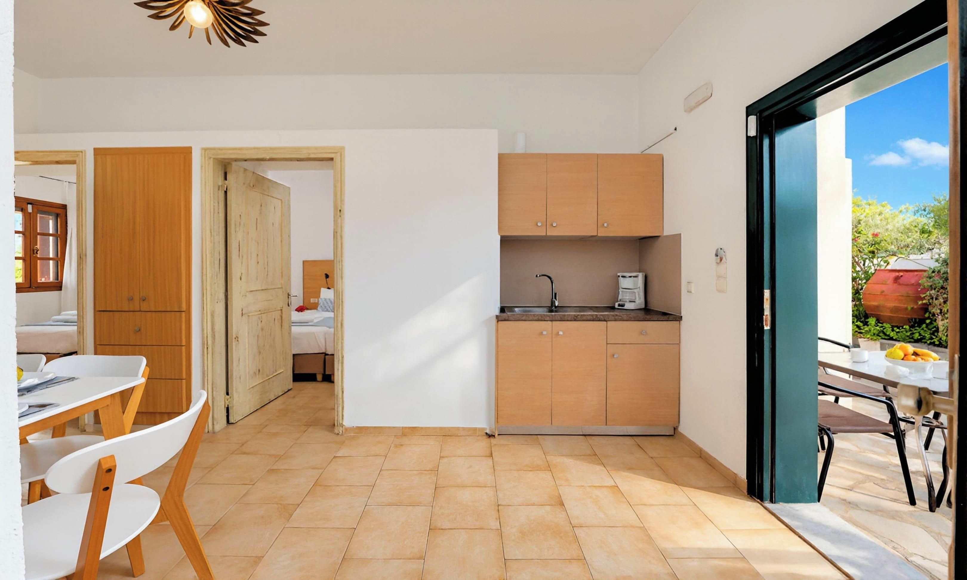 Et lille køkken med vask, skabe og et spiseområde med stole og bord.