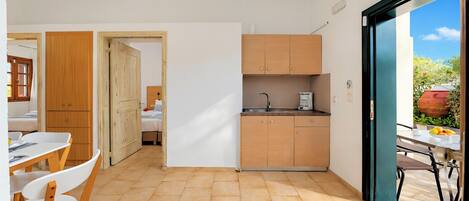 Cocina compacta con lavamanos, armarios y una zona de comedor con sillas y mesa.