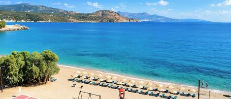 A beach with clear blue water, a row of sun loungers, and a lifeguard tower.
