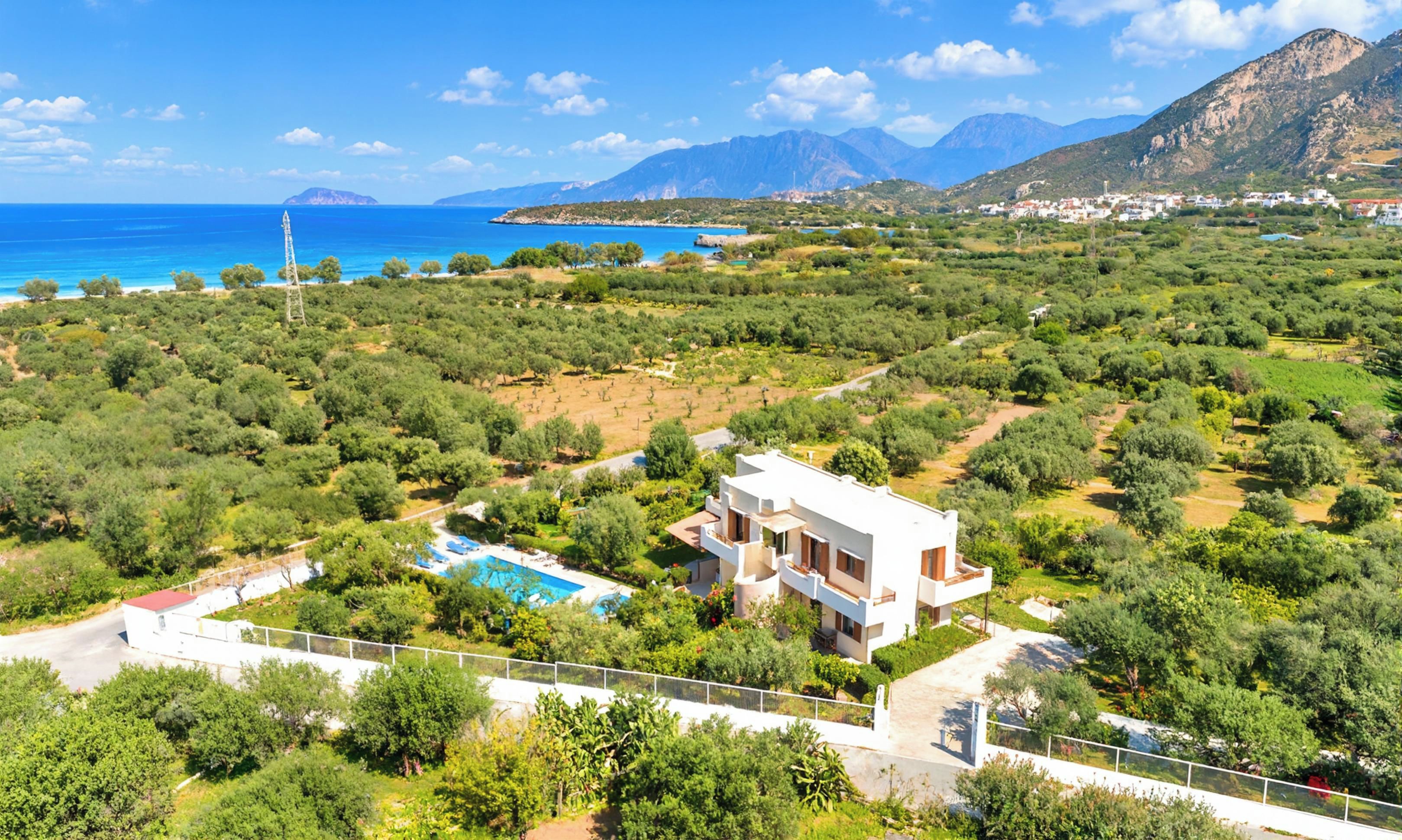 A modern villa with a pool, surrounded by lush greenery and a view of the sea and mountains.