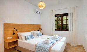 A double bed with a wooden headboard, bedside tables, and a window with curtains. - Plaisir Beachside Apts (Agios Nikolaos)