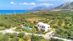 A modern villa with a swimming pool, surrounded by lush greenery and a view of the sea and mountains.