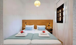 A double bed with two pillows, a bedside table with a lamp, and a window with shutters. - Plaisir Beachside Apts (Agios Nikolaos)