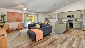 Un salon moderne comprenant un canapé, un pouf et des fauteuils, une cuisine équipée et un coin repas avec une table et des chaises.