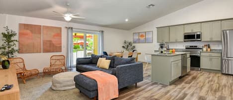 A modern living room with a sofa, ottoman, and chairs, a kitchen with appliances, and a dining area with a table and chairs.