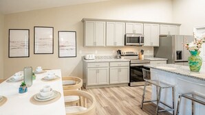 Una cocina moderna con muebles blancos, electrodomésticos de acero inoxidable y un comedor con una mesa blanca dispuesta para cuatro comensales.