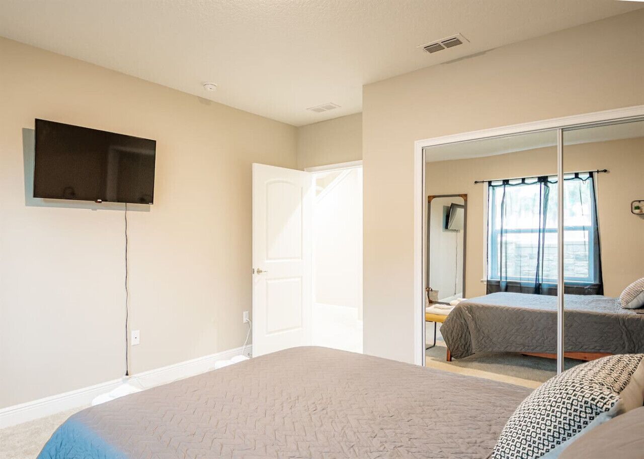 A bedroom with a bed, a TV mounted on the wall, and a door leading to another room.