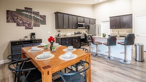 Una cocina moderna con armarios oscuros, una isla central con taburetes de bar y un comedor con mesa de madera dispuesta para cuatro personas.