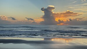 Escena de playa con olas tranquilas y un atardecer.