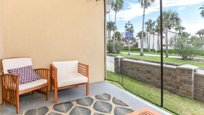 A balcony with two wooden chairs, a patterned cushion, and a view of palm trees and a building in the distance. - Beach Bliss, 5 MIN to BEACH-Game Room, Parking, AC (Daytona Beach Shores)