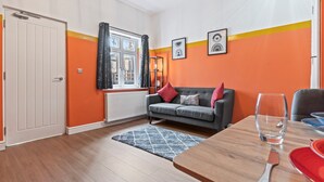 Un salon moderne avec un canapé gris, des murs orange et une table à manger en bois, sur laquelle se trouvent un verre et un couteau.