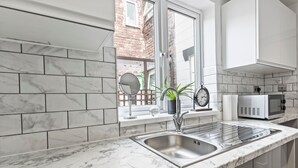 Une cuisine moderne dotée d’un plan de travail en marbre, d’un évier en acier inoxydable et d’une fenêtre donnant sur un bâtiment en briques.