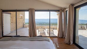 Une chambre avec un grand lit, un balcon avec une table et des chaises, et une vue sur le paysage.