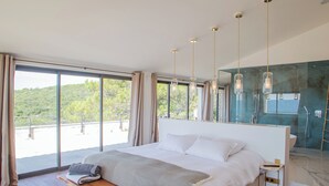 Une chambre moderne avec un grand lit, une table de chevet, un banc et une vue sur un balcon.