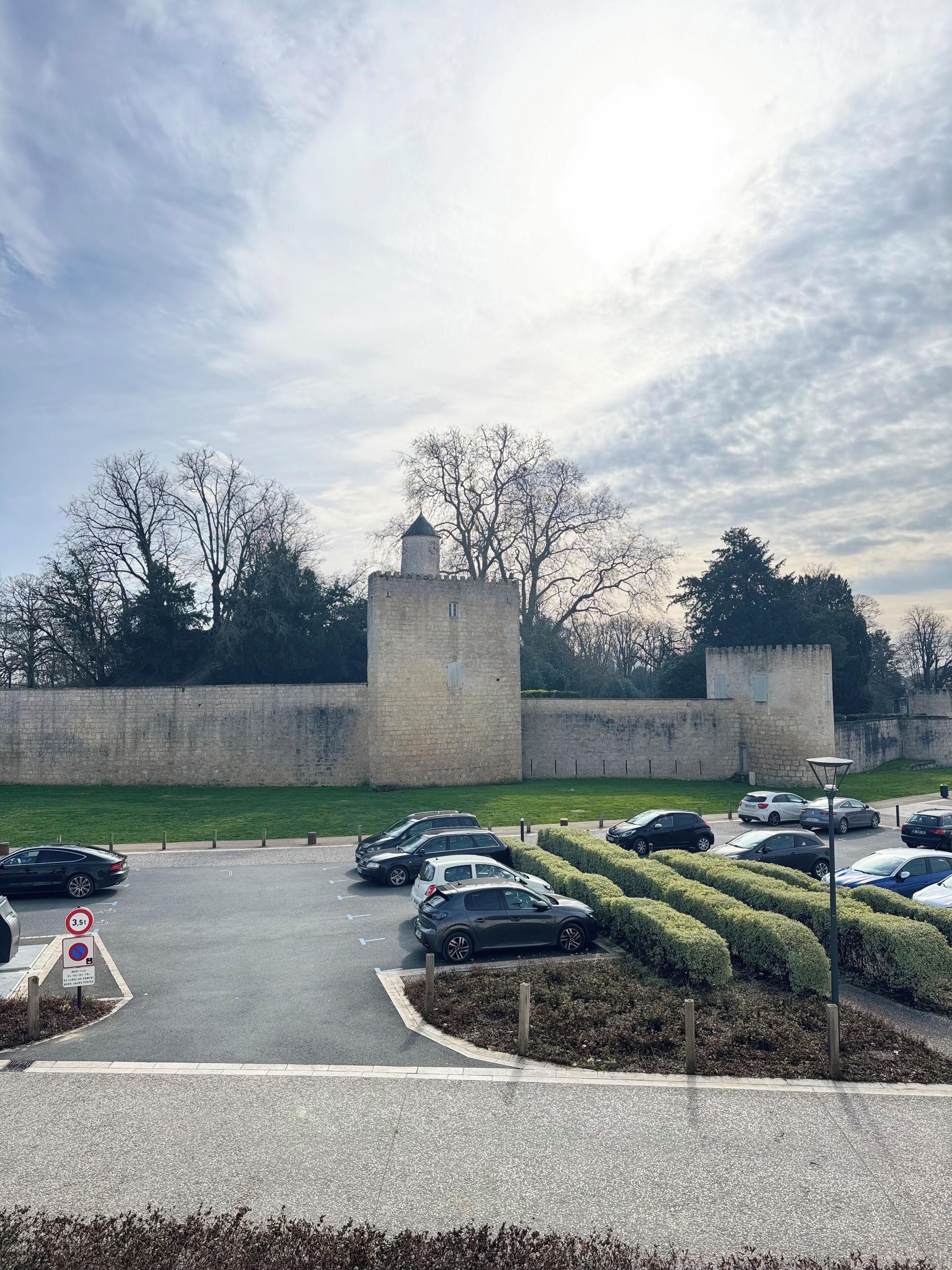 A parking area with multiple cars, a stone wall, and a tower-like structure in the background.
