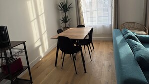 A living room with a wooden dining table, black chairs, a teal sofa, a potted plant, and a window with curtains. - Facing the castle & Air-conditioned ~ El Castillo ~ (Surgères)