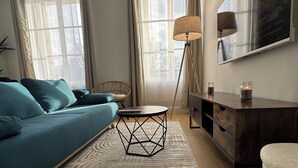 A modern living room with a sofa, a round coffee table, a floor lamp, a TV, and a painting on the wall. - Facing the castle & Air-conditioned ~ El Castillo ~ (Surgères)