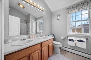 A bathroom with two sinks, a mirror, a toilet, and a window with a view of the outside.