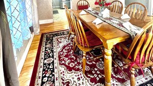 Een eetkamer met een houten tafel, rode fauteuils, een kroonluchter en een kamerbreed tapijt.