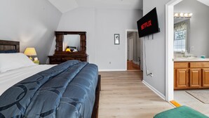 Een slaapkamer met een bed, een aan de muur bevestigde televisie en een houten dressoir.