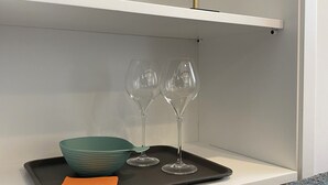 Une étagère avec un bol turquoise, deux verres à vin et un plateau sur lequel se trouve une serviette orange.