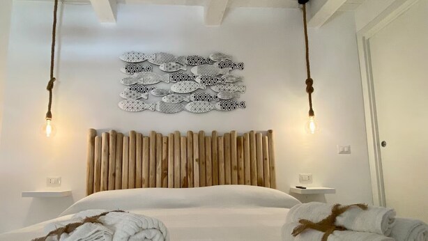 Une chambre à coucher moderne avec une tête de lit en bois, deux tables de chevet, un grand lit et des œuvres d’art décoratives au mur.