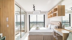 A modern bedroom with a large bed, a desk, and a balcony with a city view. - Residencial Pacobá (São Paulo)