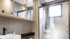 A modern bathroom with a large mirror, a white sink, a toilet, and a glass-enclosed shower area. - Residencial Pacobá (São Paulo)