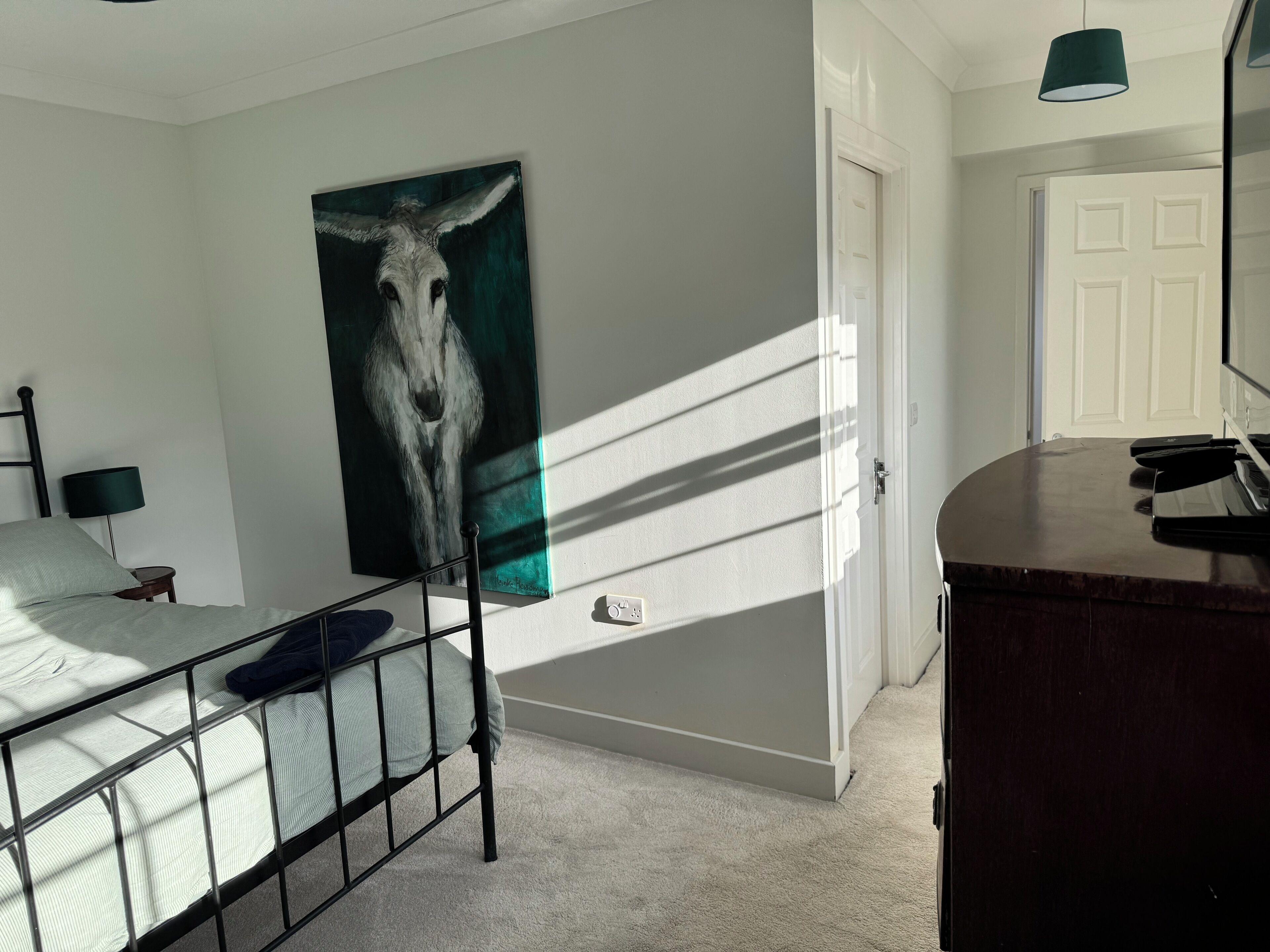 A bedroom with a bed, a painting, a desk, and a door.