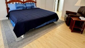 Quarto com uma cama, uma cadeira, um abajur e uma porta que dá para outro cômodo.