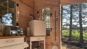 Eine kompakte Holzhütte mit einer Küchenzeile, darunter ein Toaster, ein kleiner Kühlschrank und eine Schrank mit Geschirr.