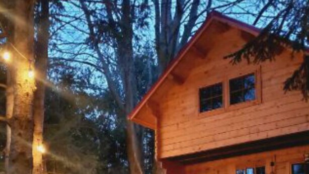 Eine Holzhütte mit Feuerstelle und Lichterkette, umgeben von Bäumen.