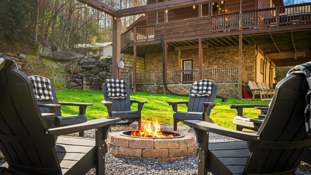 Una terraza de madera con una chimenea, rodeada de sillas Adirondack, y un edificio de piedra al fondo.