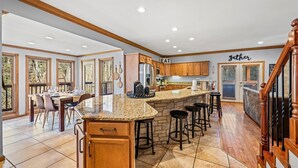 Una cocina amplia con una isla central, armarios de madera y un comedor con un gran ventanal que da a una terraza.