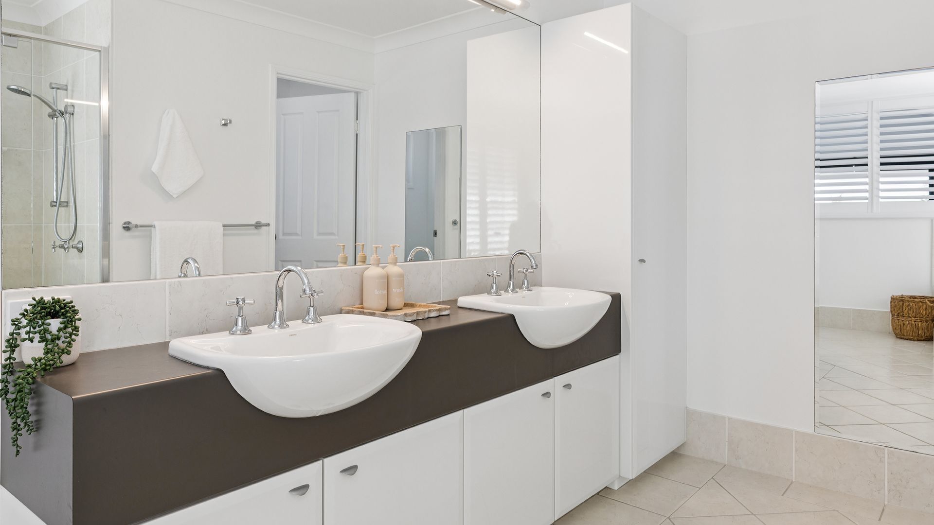 A modern bathroom with two sinks, a large mirror, and a shower area.