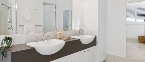 A modern bathroom with two sinks, a large mirror, and a shower area.