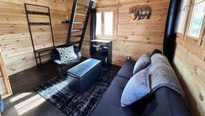 A cabin interior with a sofa, a black ottoman, a ladder, a small table, and a window. - Black Bear, Black Bear Lakefront Cabin (Cantwell)