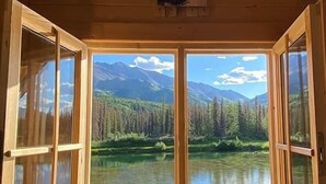 A wooden cabin with open windows revealing a mountain landscape and a lake. - Black Bear, Black Bear Lakefront Cabin (Cantwell)