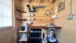 Een compacte keuken met houten wanden, een wastafel, een magnetron, een waterkoker en een kleine koelkast.