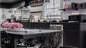 Une cuisine moderne avec un coin repas, caractérisée par une palette de couleurs en noir et blanc, des appareils en acier inoxydable et des éléments décoratifs tels que des verres colorés et un vase de fleurs.