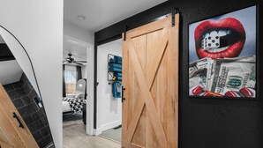 Un couloir avec une porte coulissante en bois, un tapis à motifs noir et blanc et une œuvre d’art murale représentant des lèvres rouges et des dés.