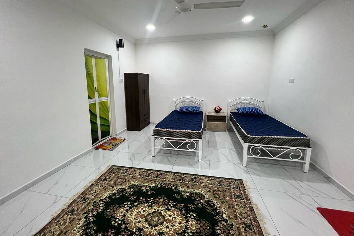Une chambre avec deux lits simples, une armoire, une petite table et un tapis décoratif.