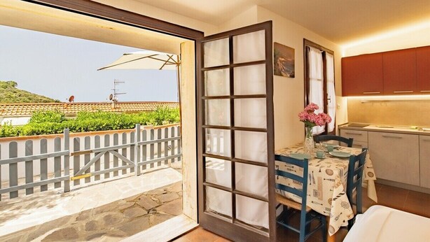 Ein Zimmer mit Balkon, einem Essbereich mit Tisch und Stühlen sowie einer Küchenzeile mit Schränken.