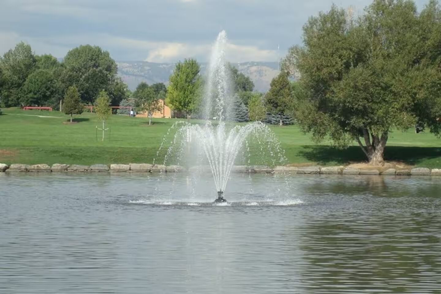 Een fontein in een park, met een gazon en bomen op de achtergrond.