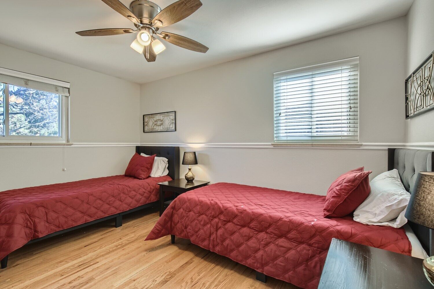 A bedroom with two beds, a ceiling fan, a nightstand with a lamp, and a window with blinds.