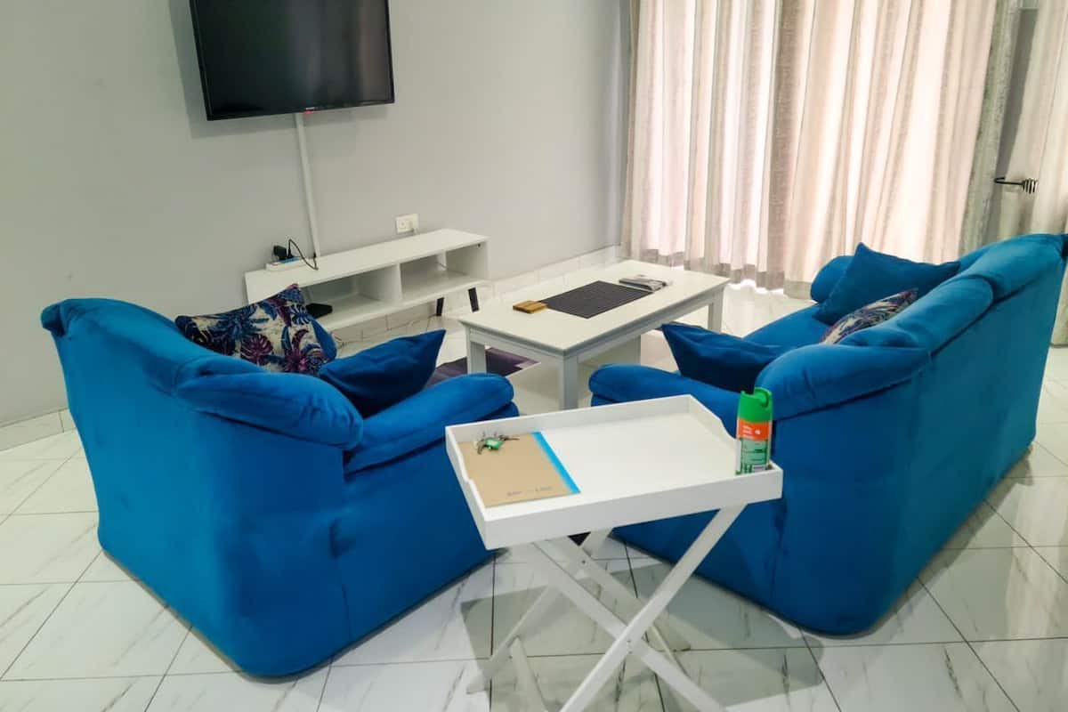 Una sala de estar moderna con sofás azules, una mesa de centro blanca y un televisor de pantalla plana montado en la pared.