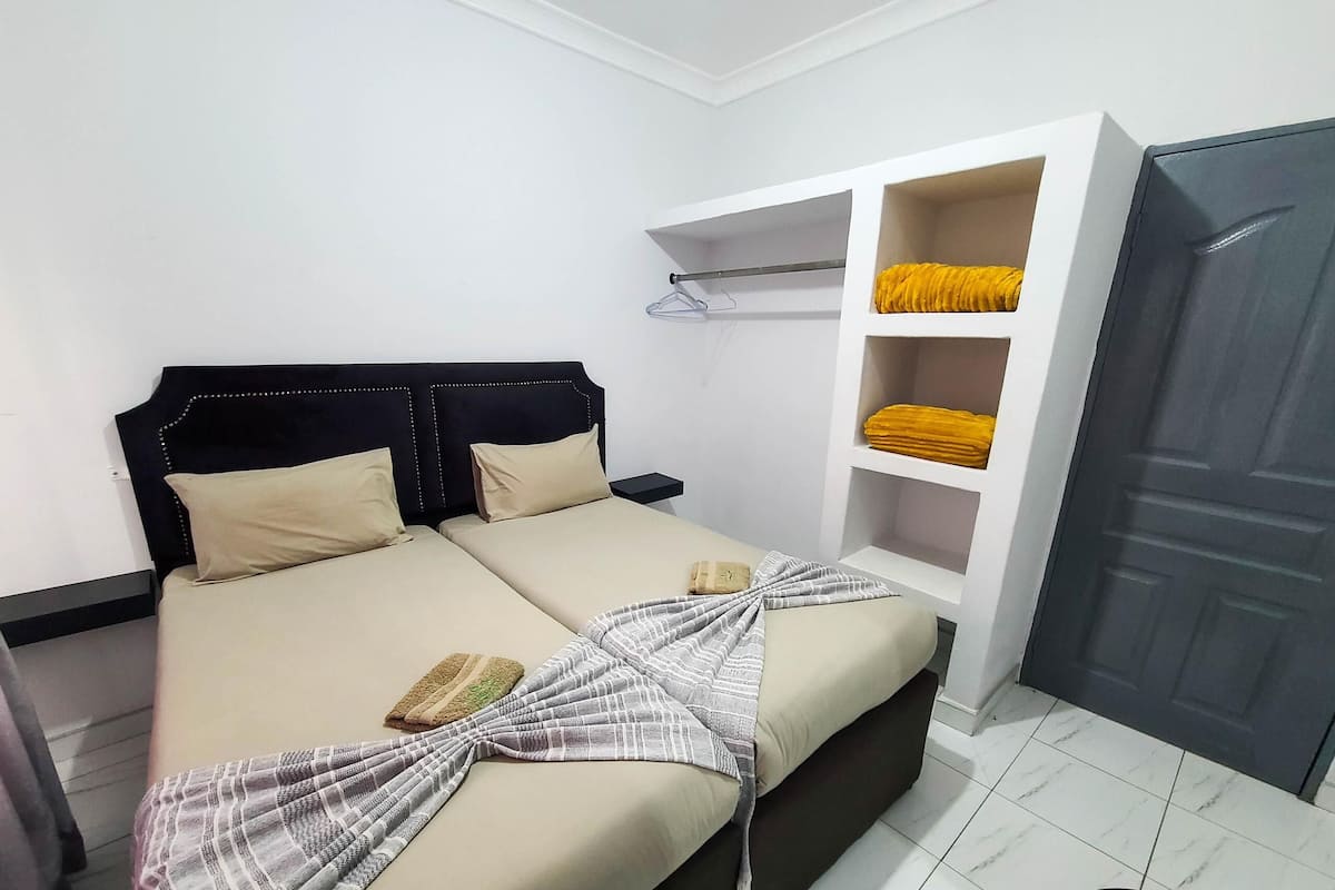Un dormitorio con cama, mesita de noche, armario y estante con ropa doblada.