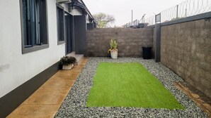 Une cour avec une pelouse verdoyante, des plantes en pot et un mur en béton.